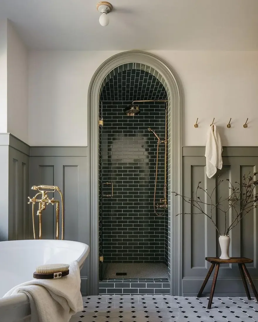 Arched shower with dark green subway tile, brass fittings and soft light