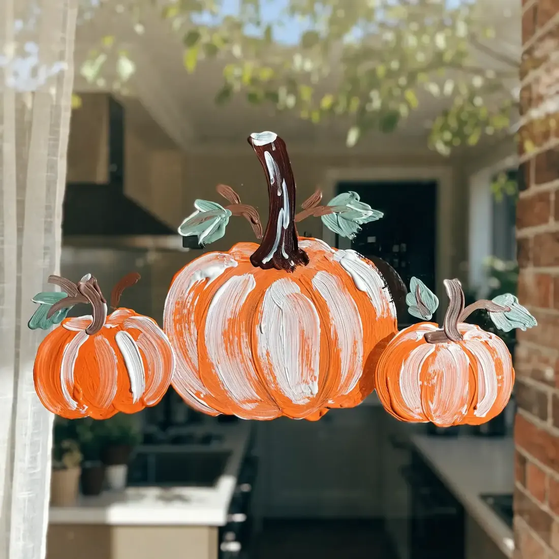 Three painted pumpkins in loose brushstrokes on a kitchen window