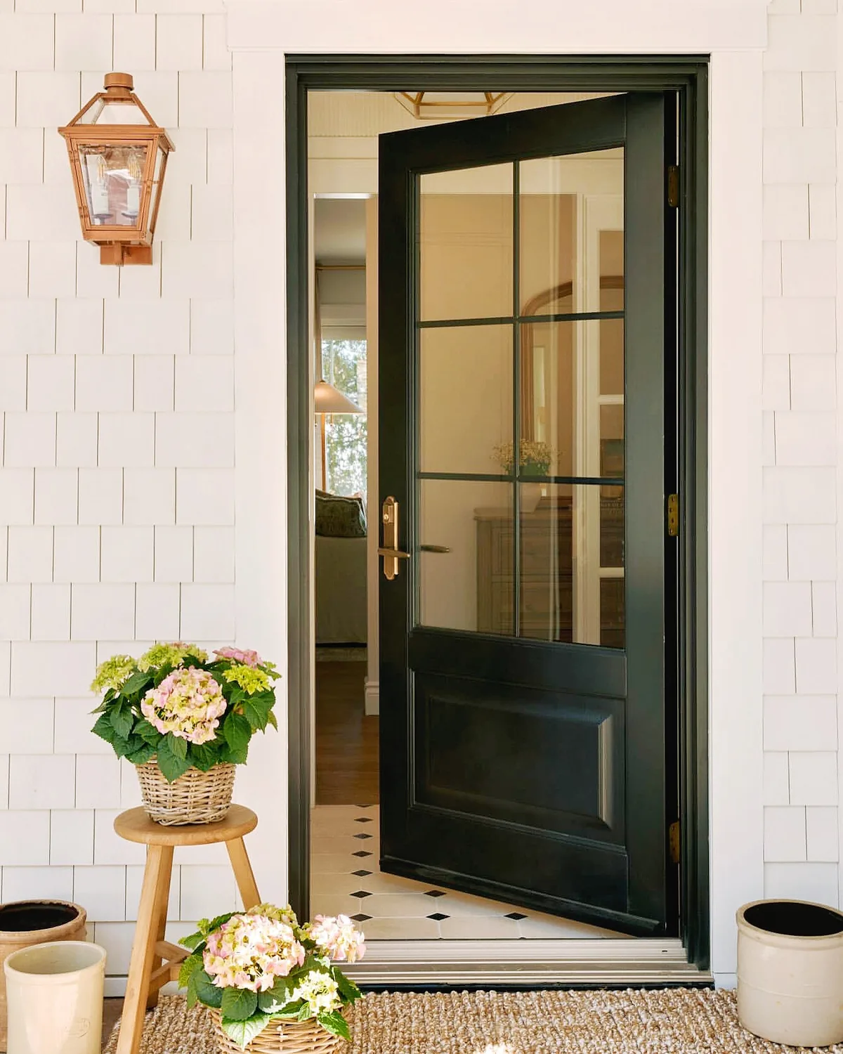 Black front door on white shingle with a lantern beside it