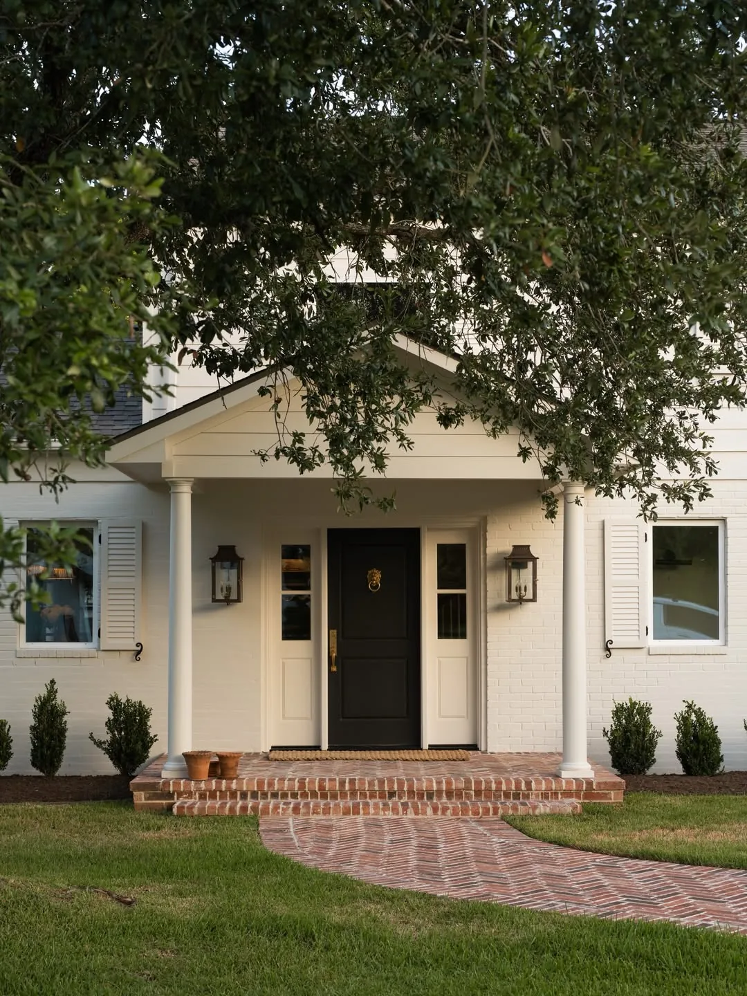 Cream house with a black door and a brick walkway leading in