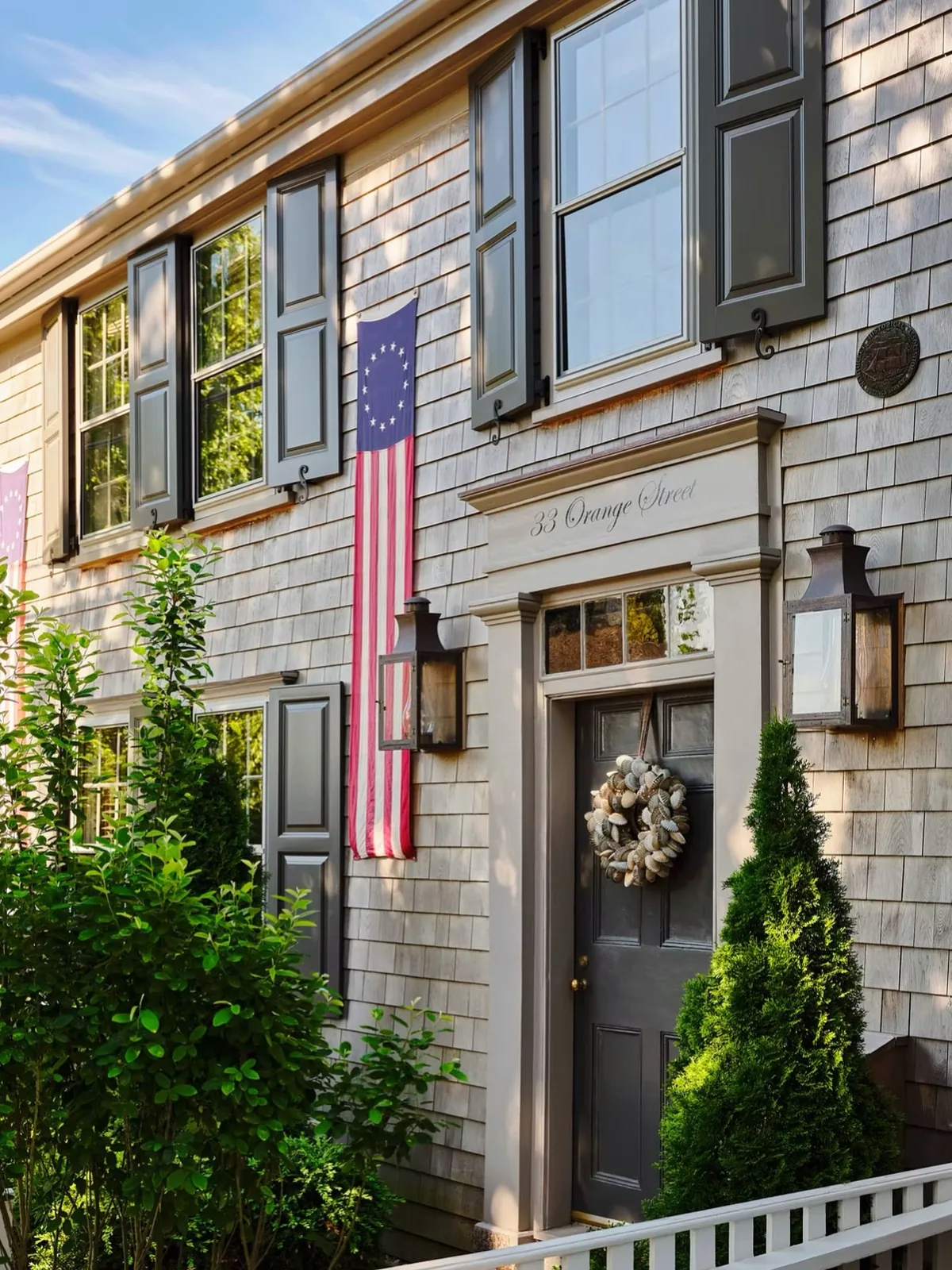 Gray shingle townhouse with a black door and twin lanterns