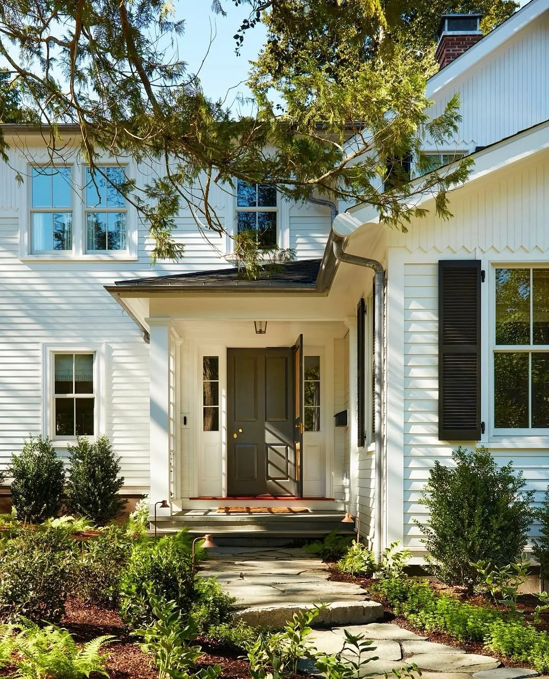 White clapboard entry with a black door beside a stone path