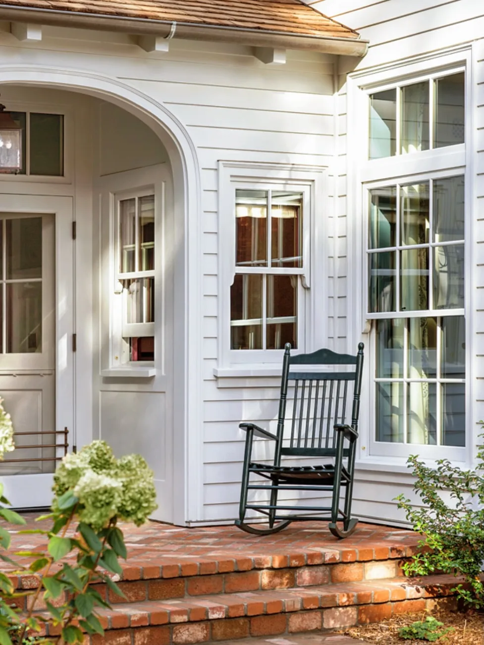 White cottage porch with a black rocking chair by the door