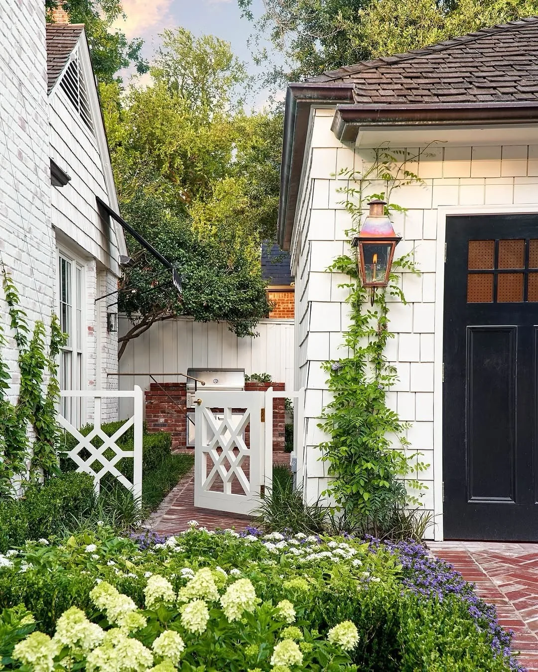 White shingle cottage with a black door and a garden gate