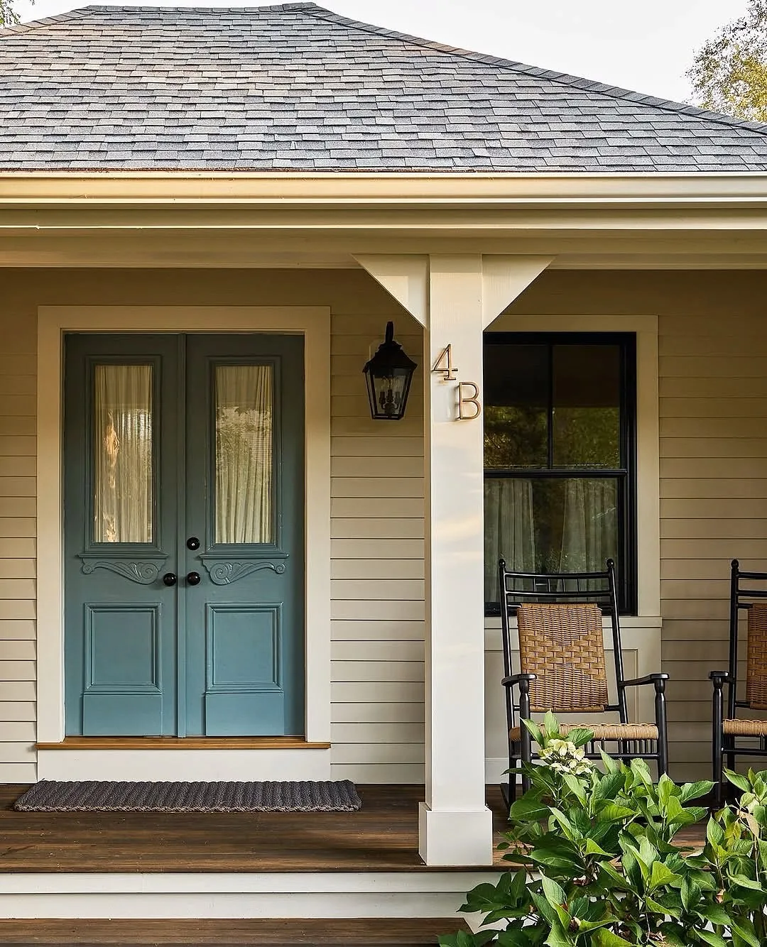 Cream cottage with blue double doors and rocking chairs on the porch
