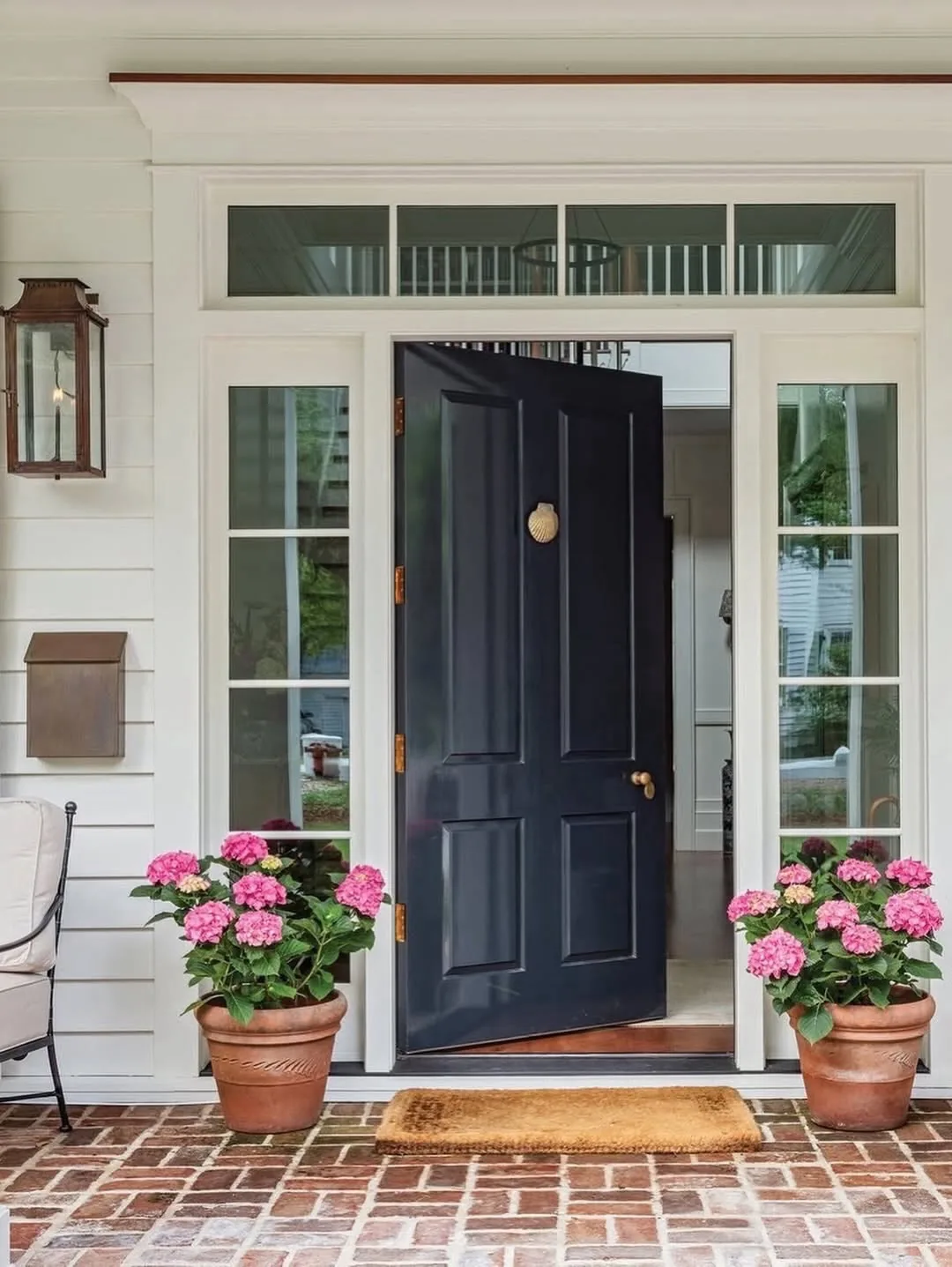 Navy blue front door on a brick porch with hydrangeas alongside