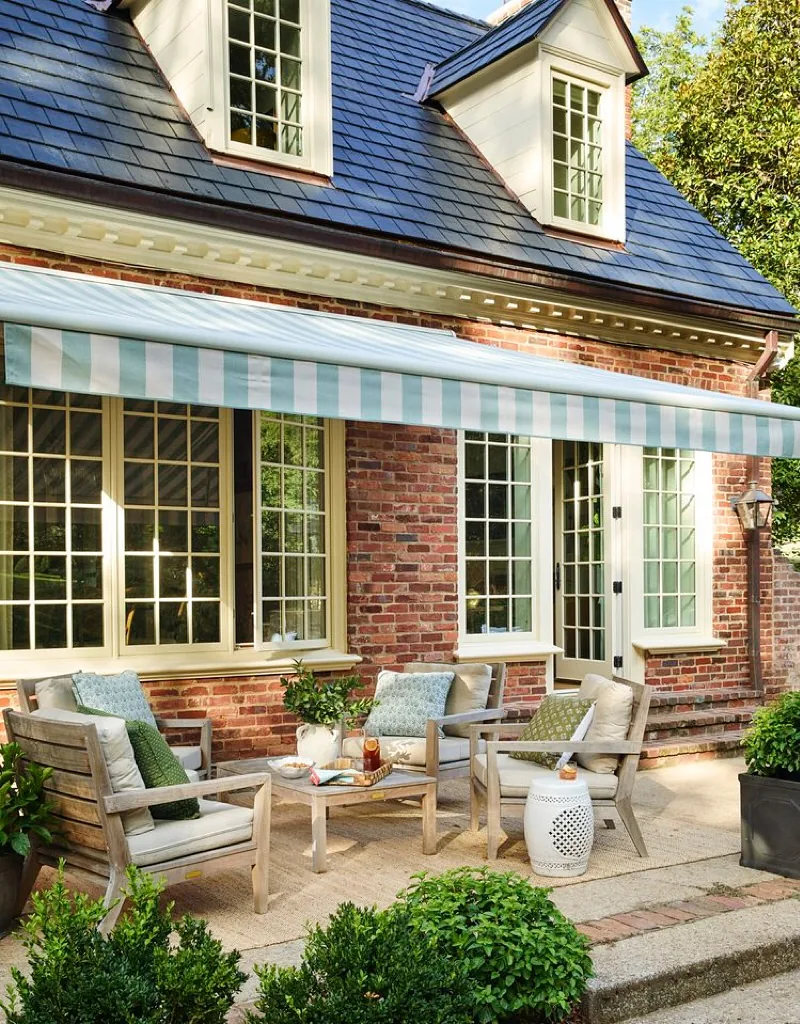 Red brick porch with a striped awning and teak seating