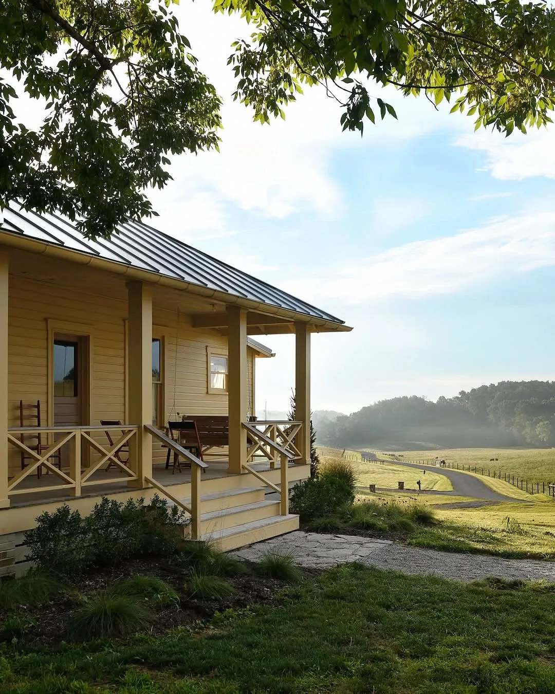 Yellow farmhouse porch with a metal roof over a wildflower meadow