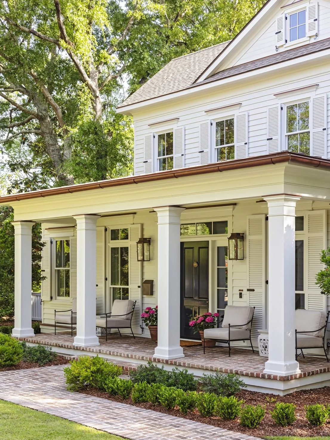 Cream columned porch with a brick path and seating