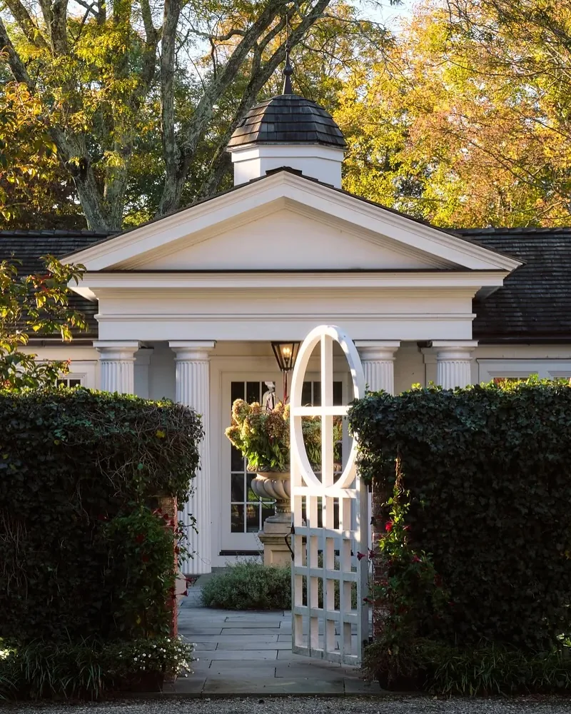 Greek Revival portico with an oval window and trimmed hedges
