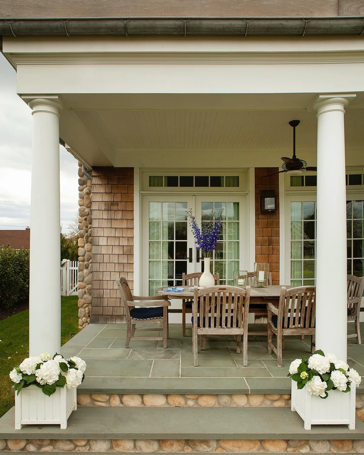 Stone column porch with teak dining and hydrangeas alongside