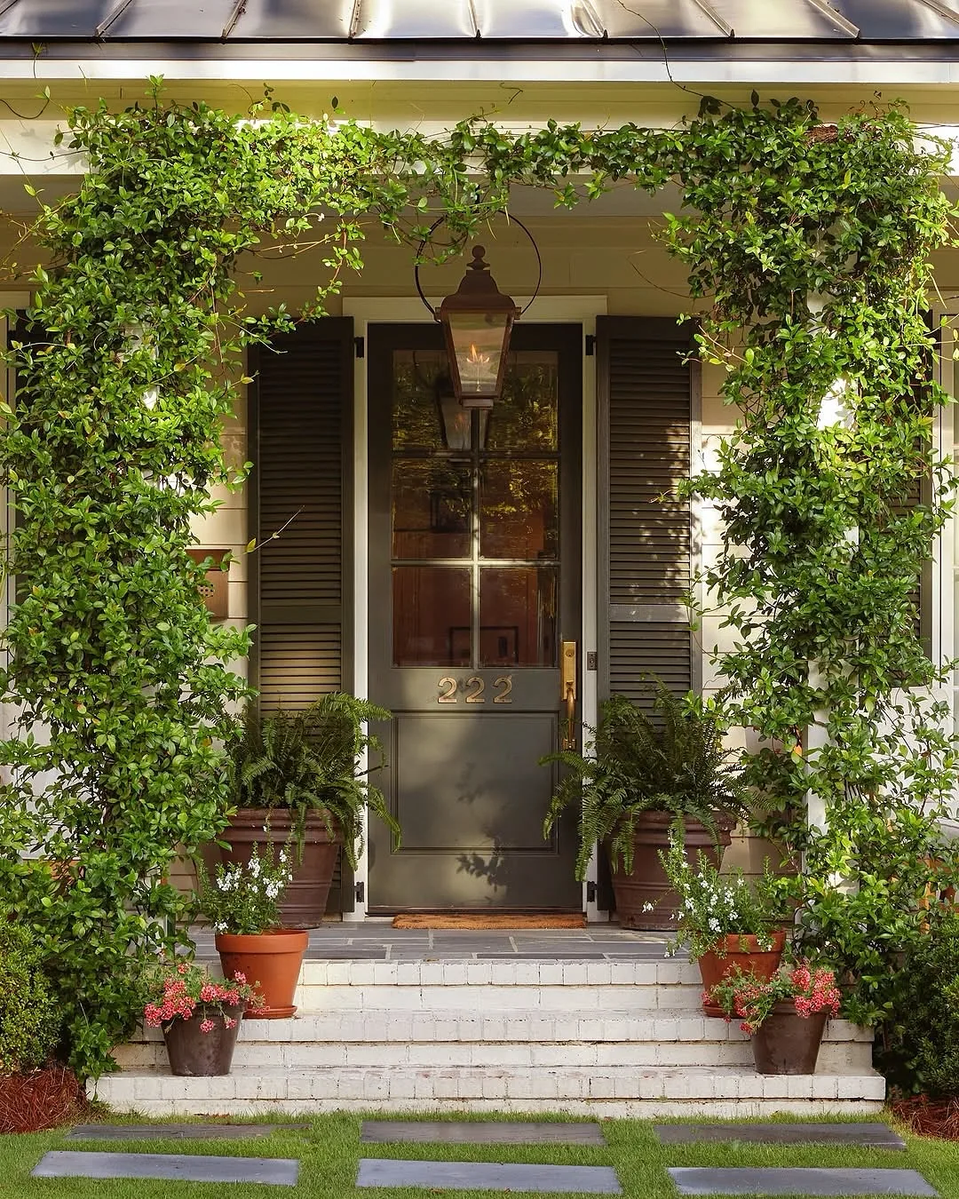 Vine-covered portico with a bronze front door behind the green