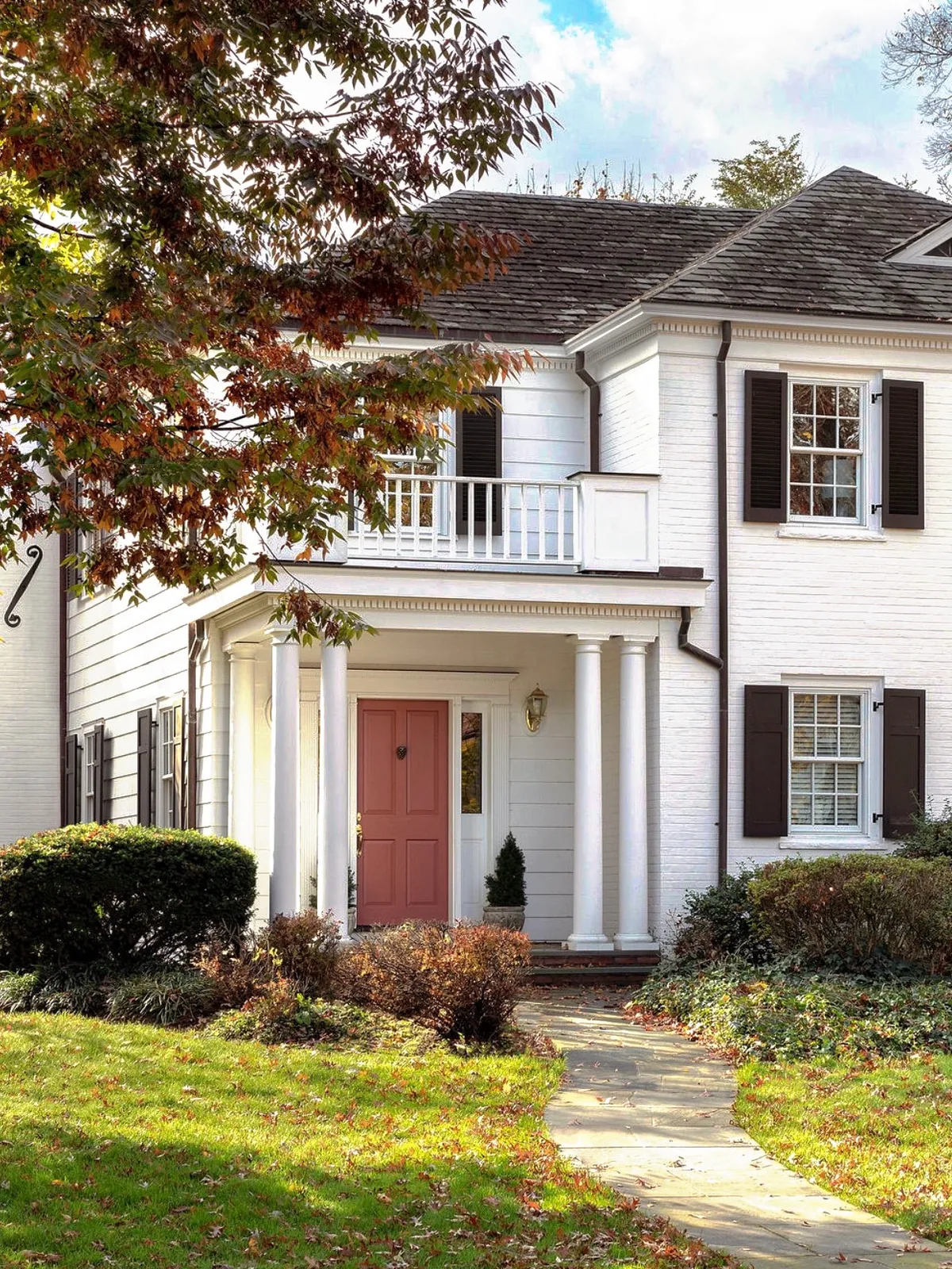 White brick colonial with columns and a pink door at the center