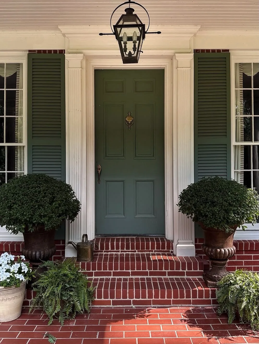 Green door with brick steps and boxwood urns flanking the entry