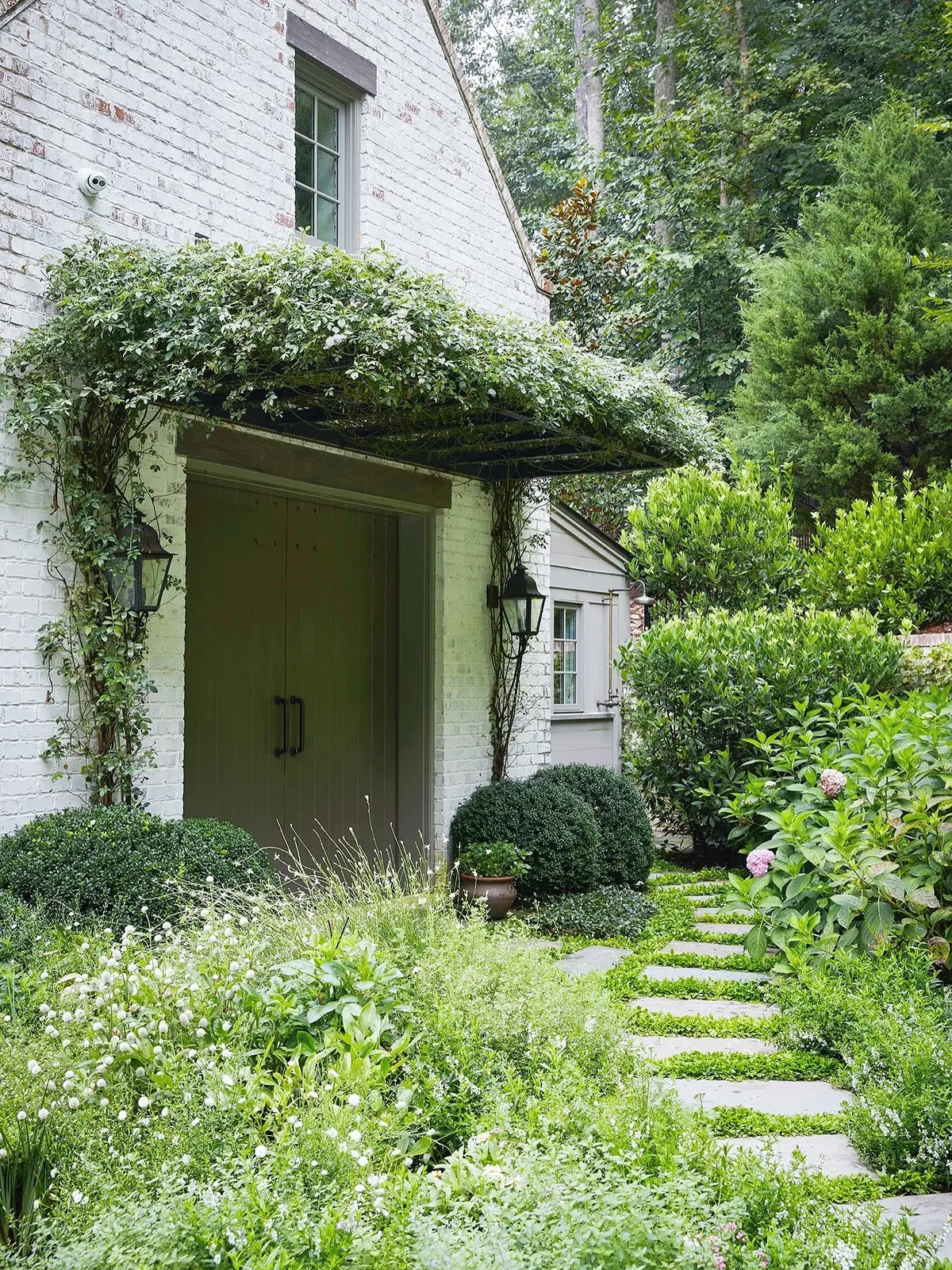 Green double doors under a vine-covered pergola at the entry