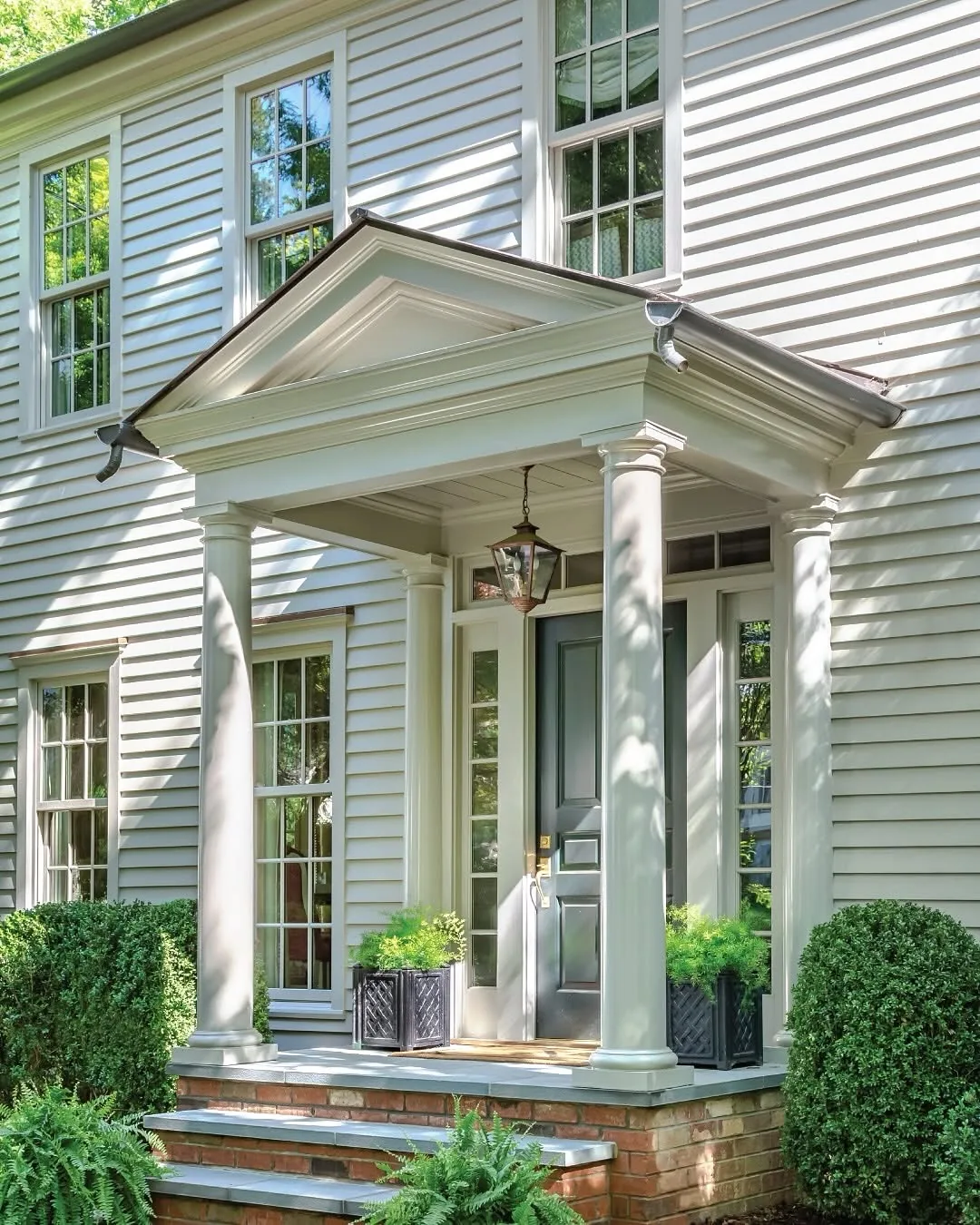 Pale green clapboard entry with a columned portico and brick path