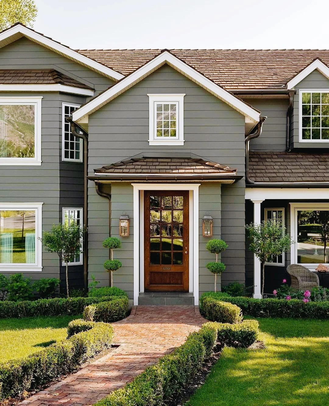 Gray clapboard house with a wood door and clipped boxwood