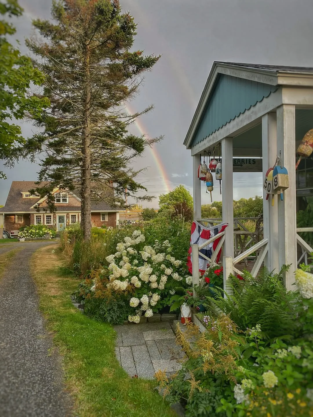 White porch with hydrangeas along a gravel drive marked by buoys