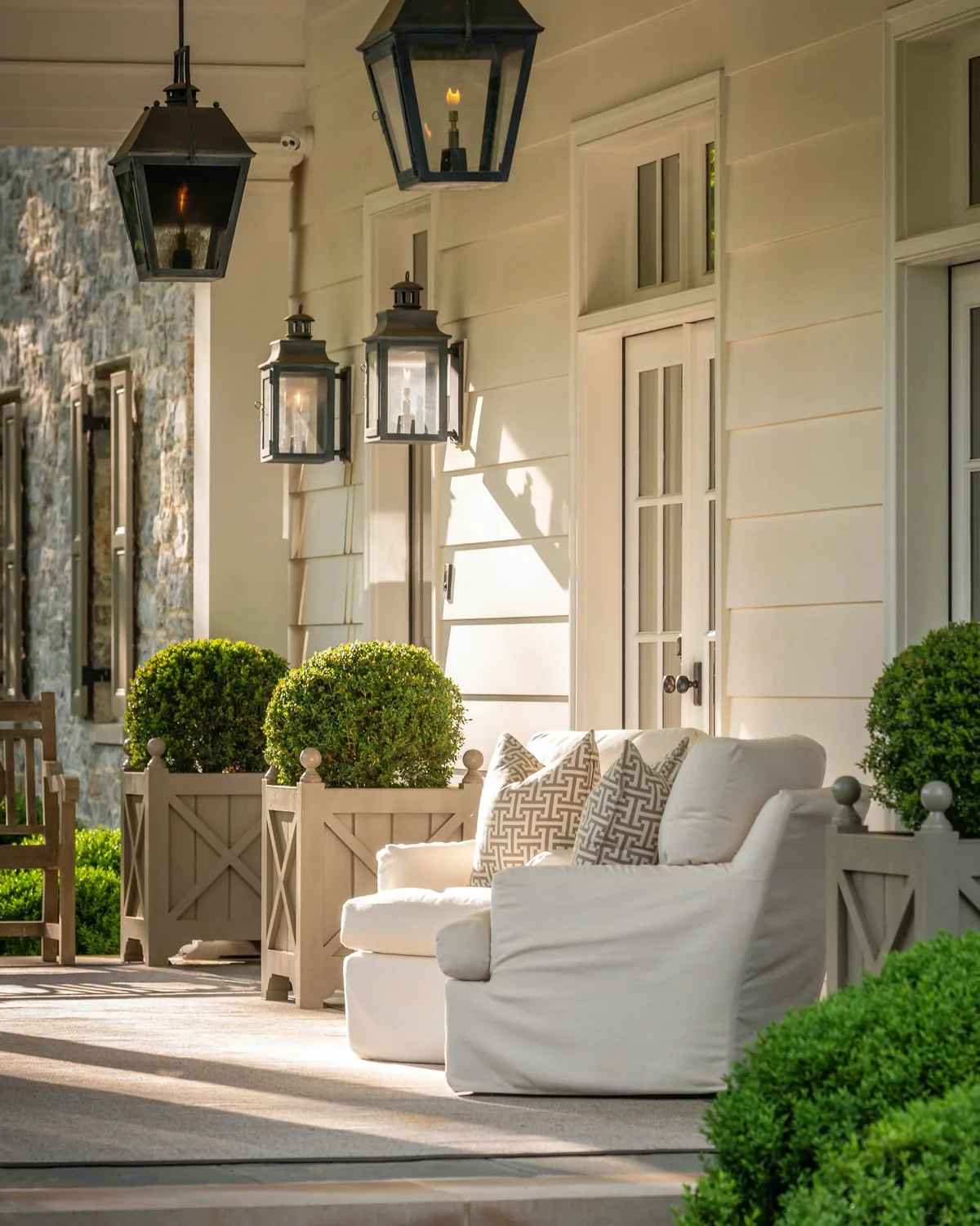 Covered porch with lanterns, white armchairs and clipped topiary