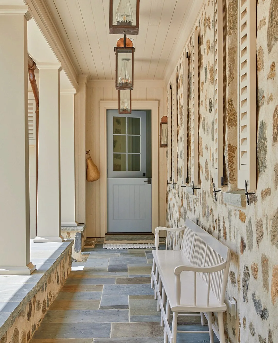 Stone farmhouse porch with a white bench beside the door