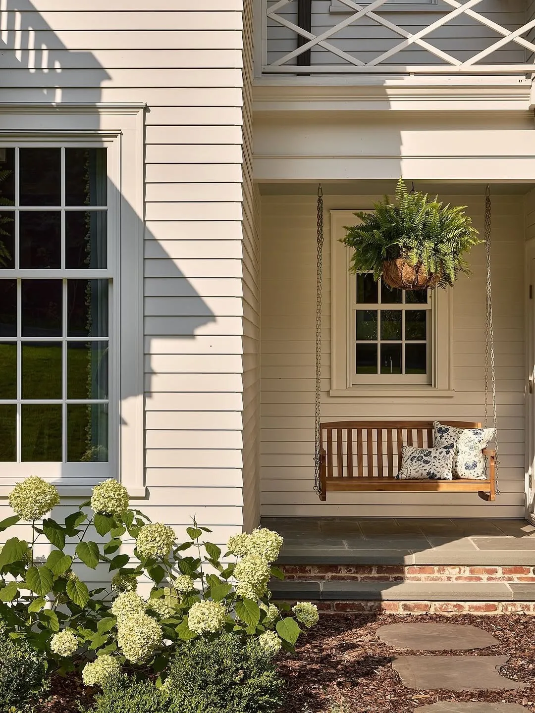 White clapboard porch swing with hydrangeas alongside