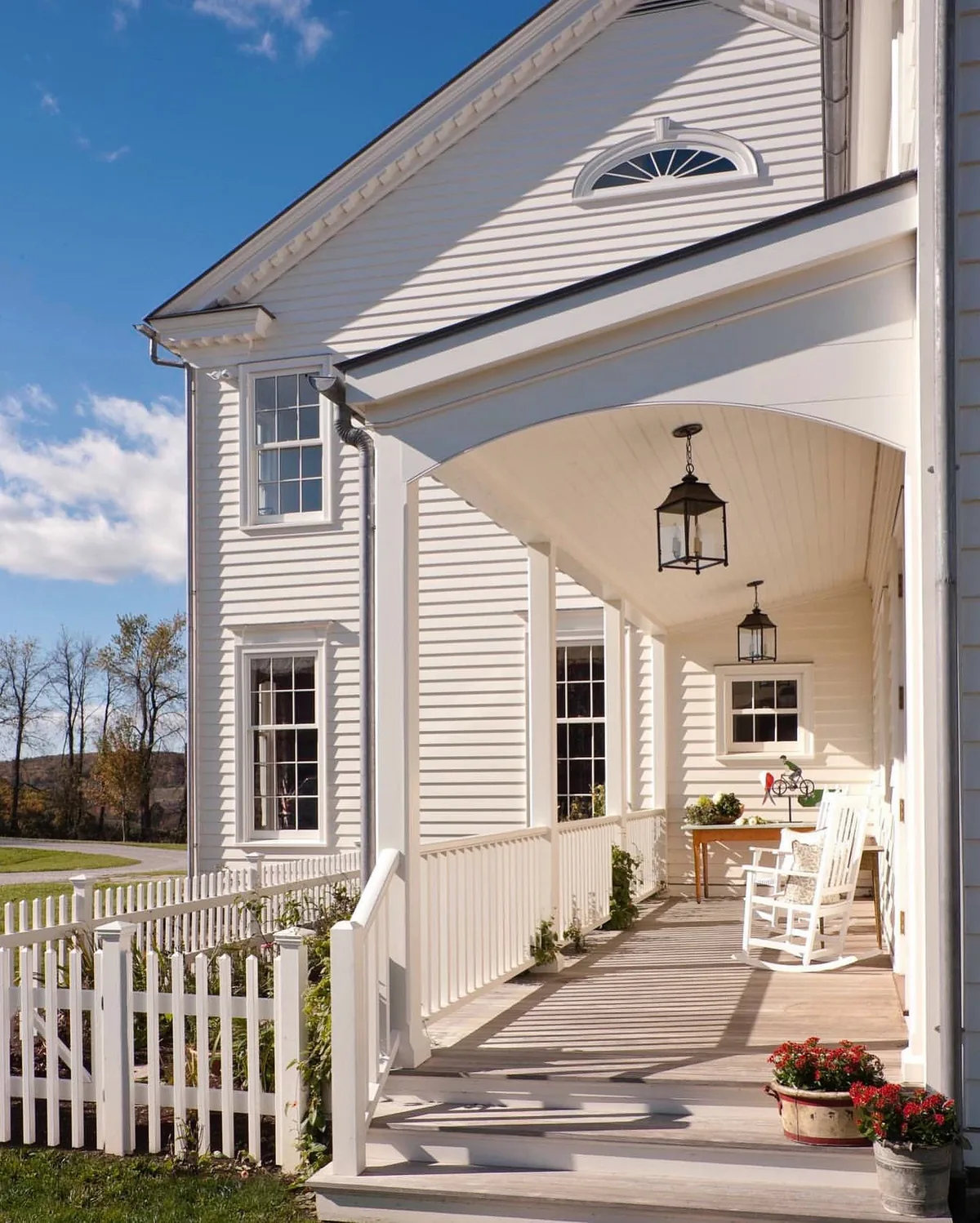 White porch with a lantern, picket fence and rockers at dusk