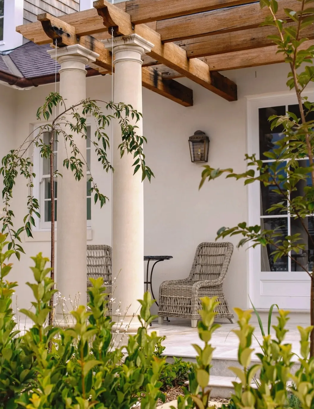 White stucco porch with a wood pergola and wicker seating