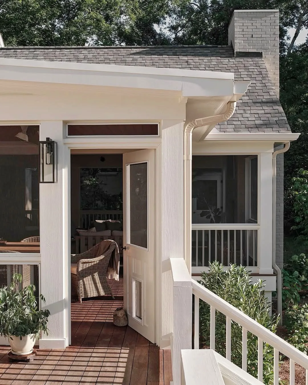 White screened porch under a shingle roof opening onto a deck