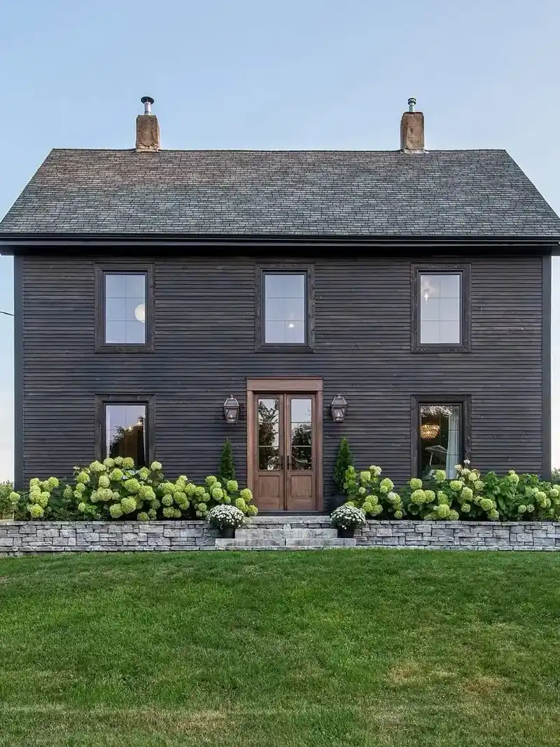 Black farmhouse exterior with stone retaining wall and lime hydrangeas along the front