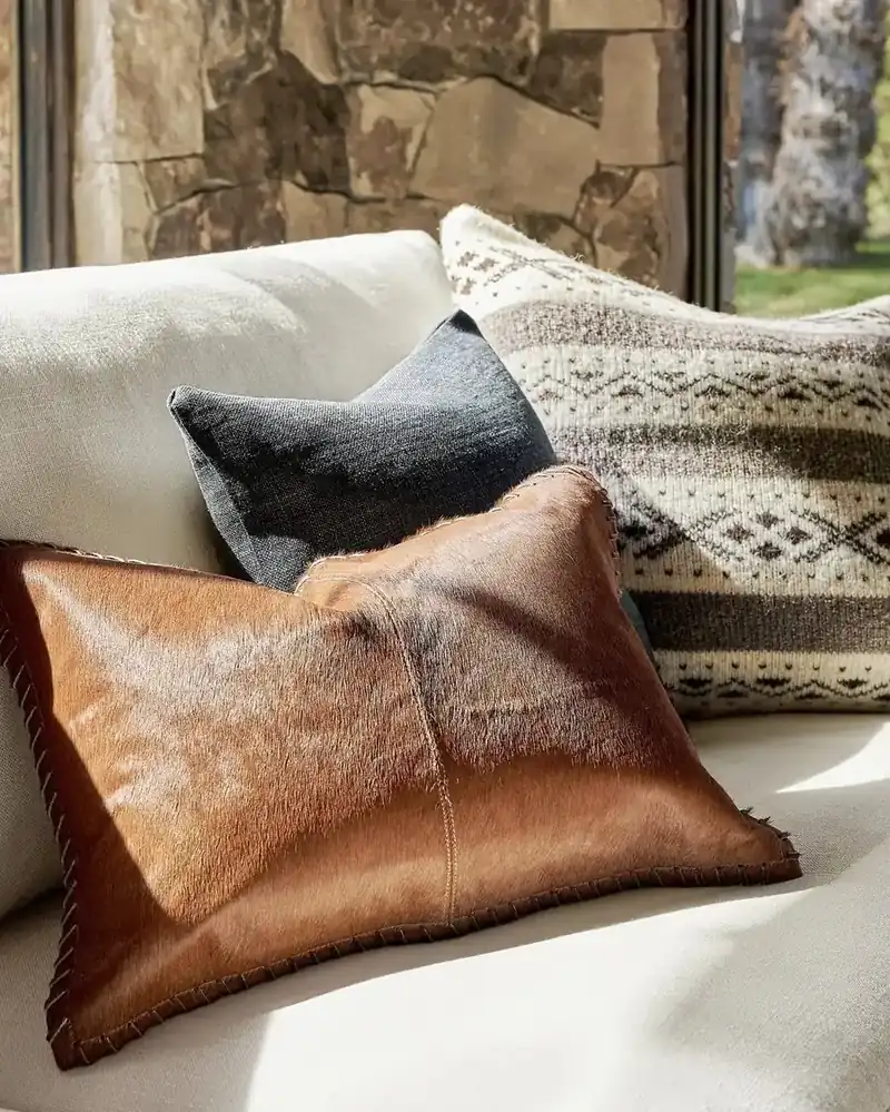 Cognac hair-on-hide pillow layered with wool and linen cushions on a cream rustic sofa