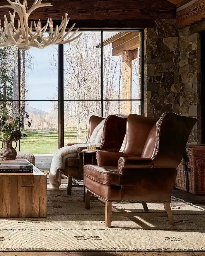 Two cognac leather wingback chairs with shearling throws in a rustic stone living room with antler chandelier