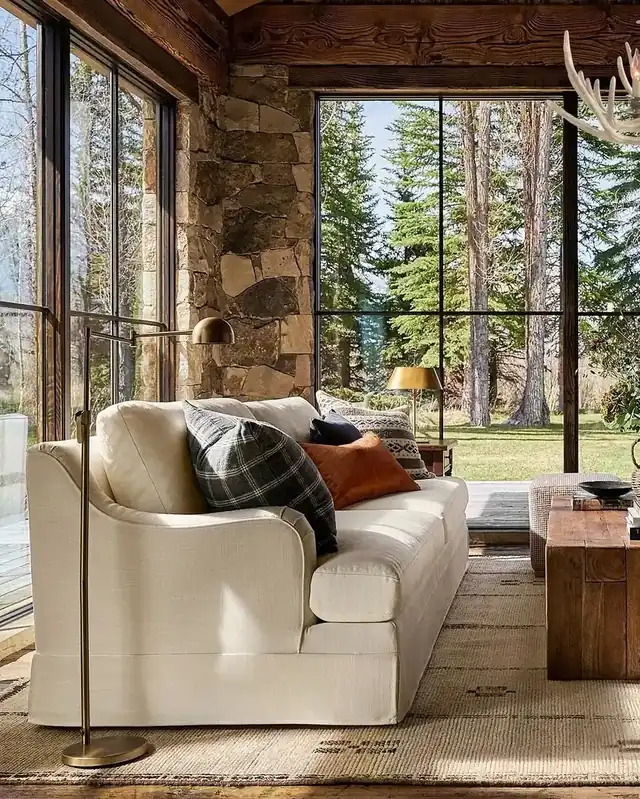 Warm rustic living room with cream linen sofa against natural stone walls and layered neutral pillows