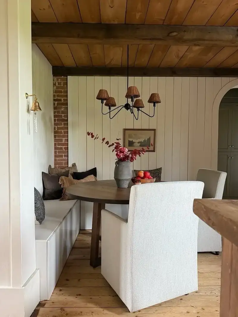 Vaulted dining area with exposed wood beams and a cozy banquette beside a brick accent wall