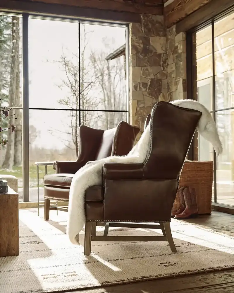Cognac leather reading chair with a soft shearling throw beside tall windows and a stone wall