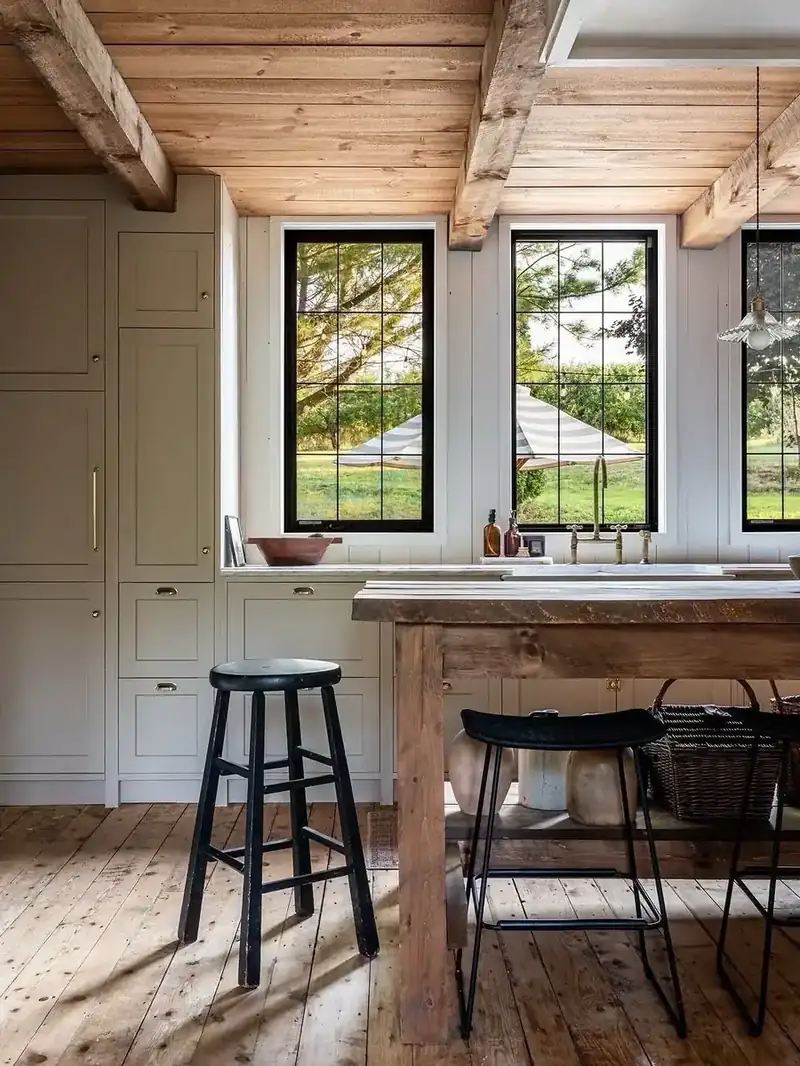 Rustic kitchen with reclaimed wood island, black stools, and brass fixtures beneath exposed beams