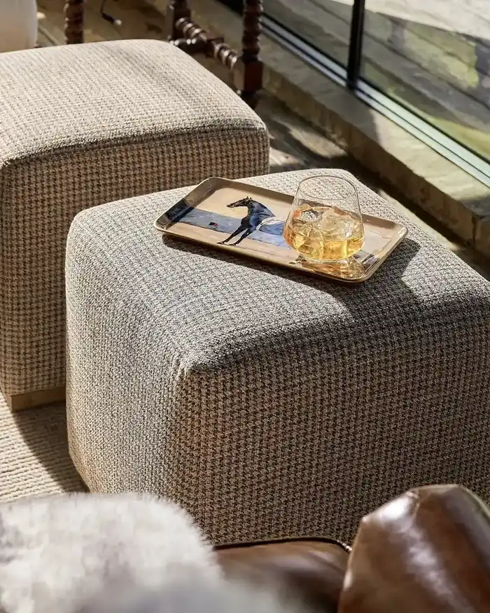 Textured boucle ottomans styled with a brass horse tray and a glass near black-framed windows