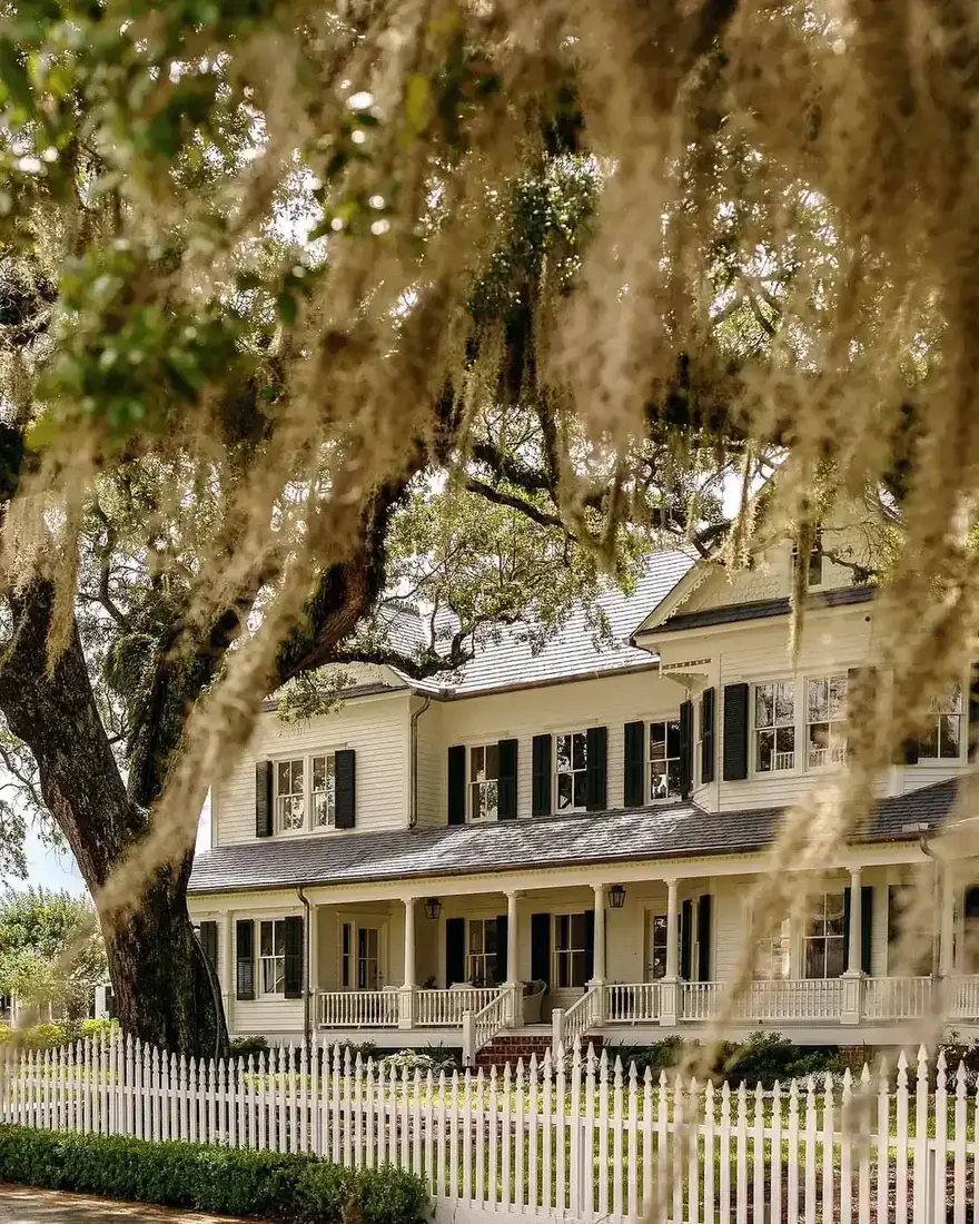 Cream clapboard house with black shutters and white picket fence