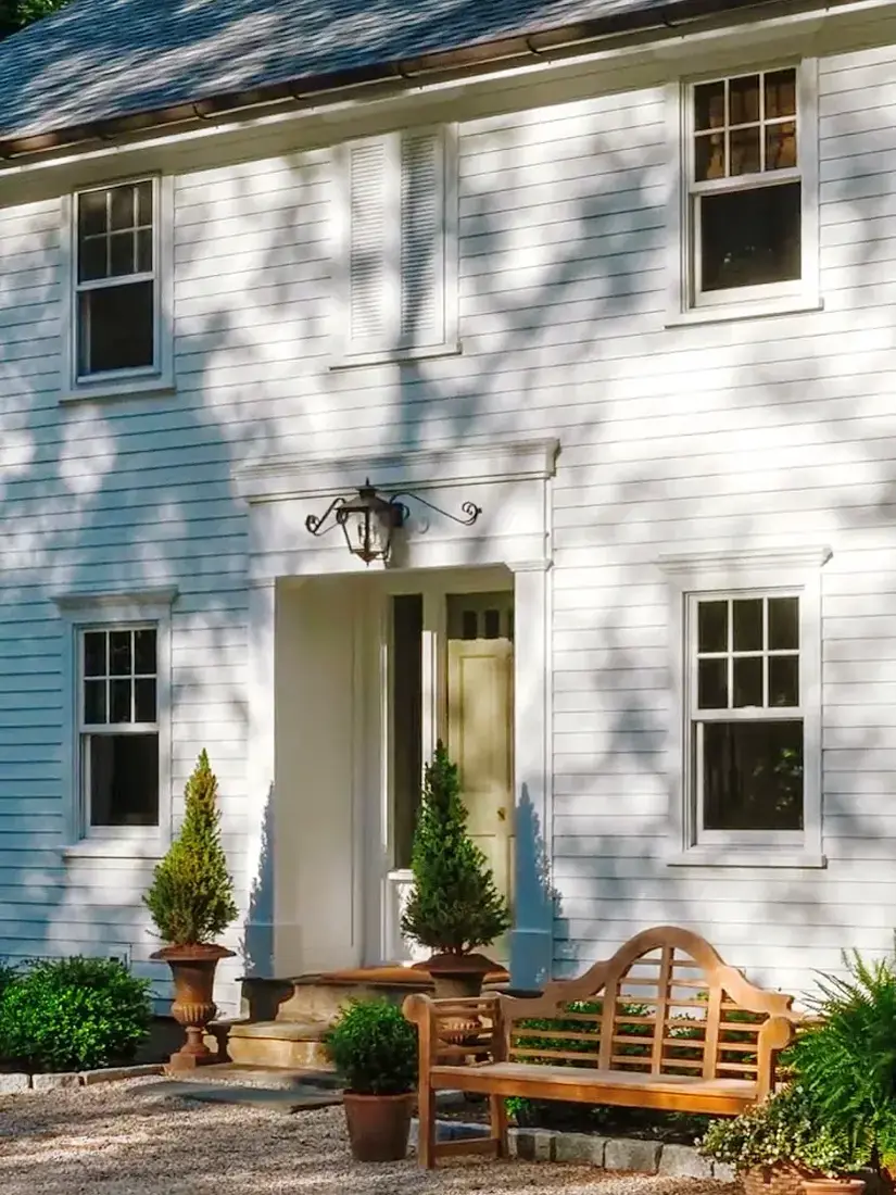White clapboard house with blue front door and teak bench by the entrance
