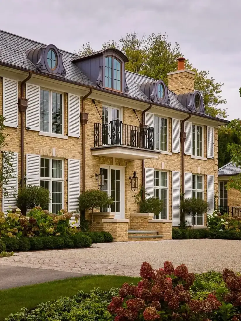 Brick manor house with copper dormers and a wrought iron balcony above the front door