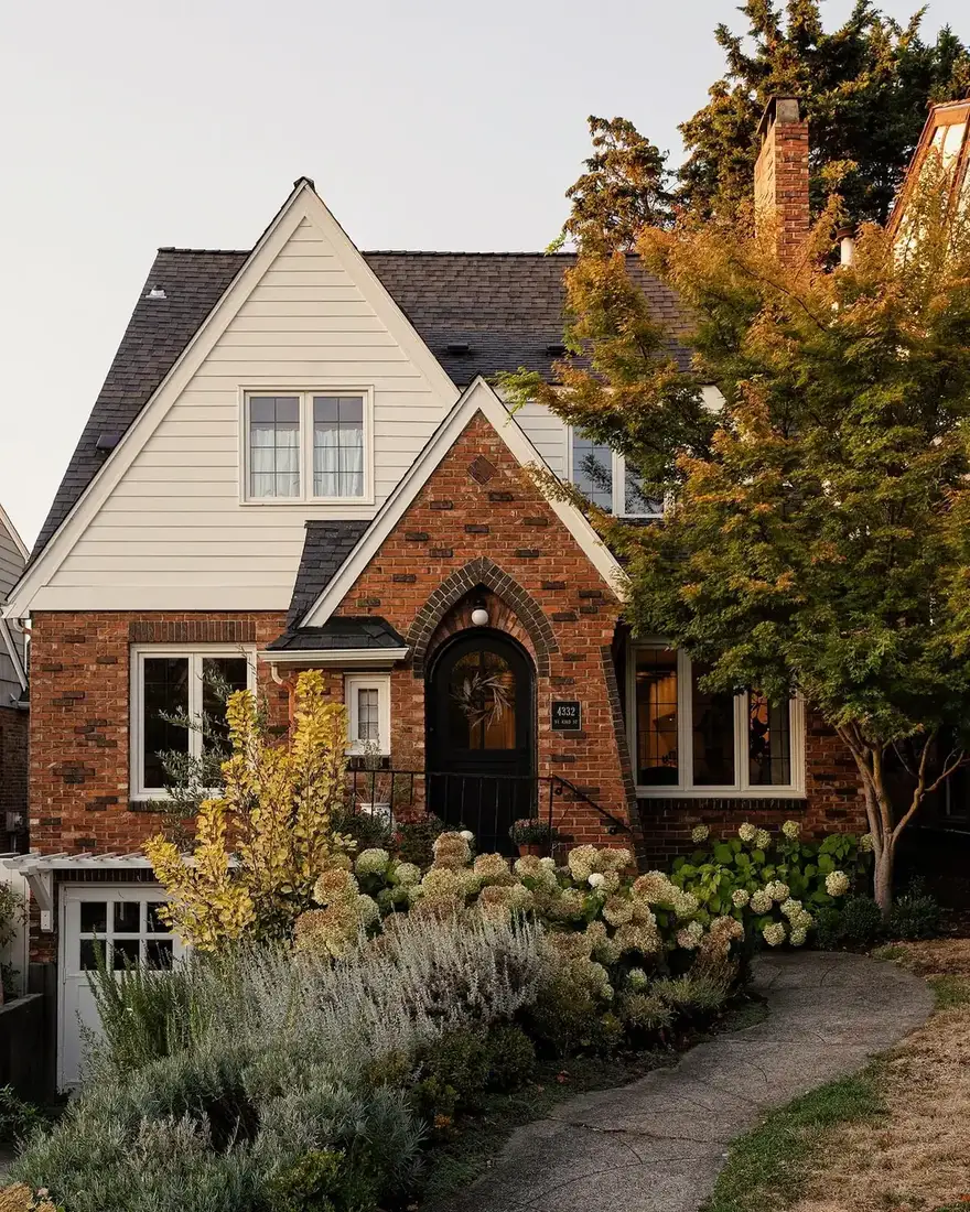Brick Tudor cottage with an arched front door and blue hydrangeas along the wall