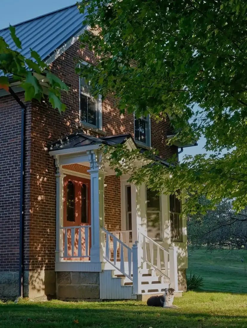 Dark brick farmhouse with a white columned porch and pale stone entry steps