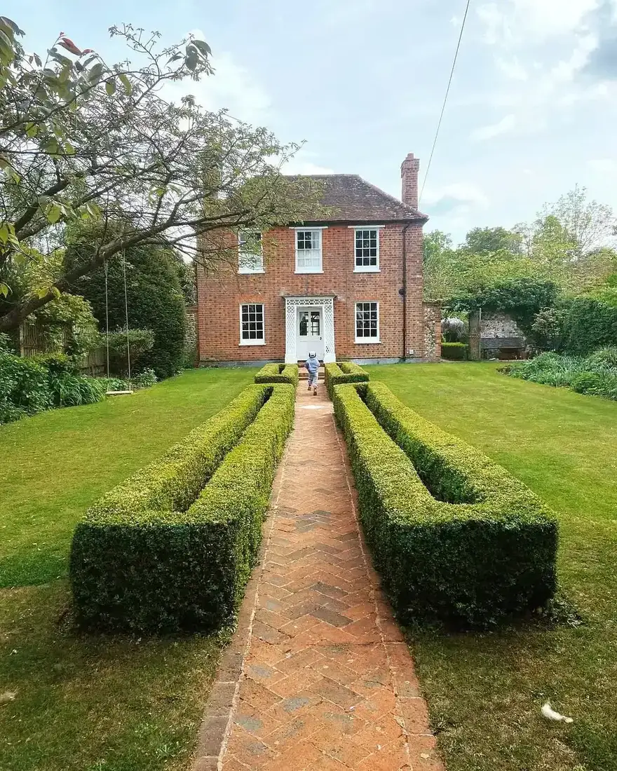 Red brick Georgian house with white trim and a clipped boxwood path