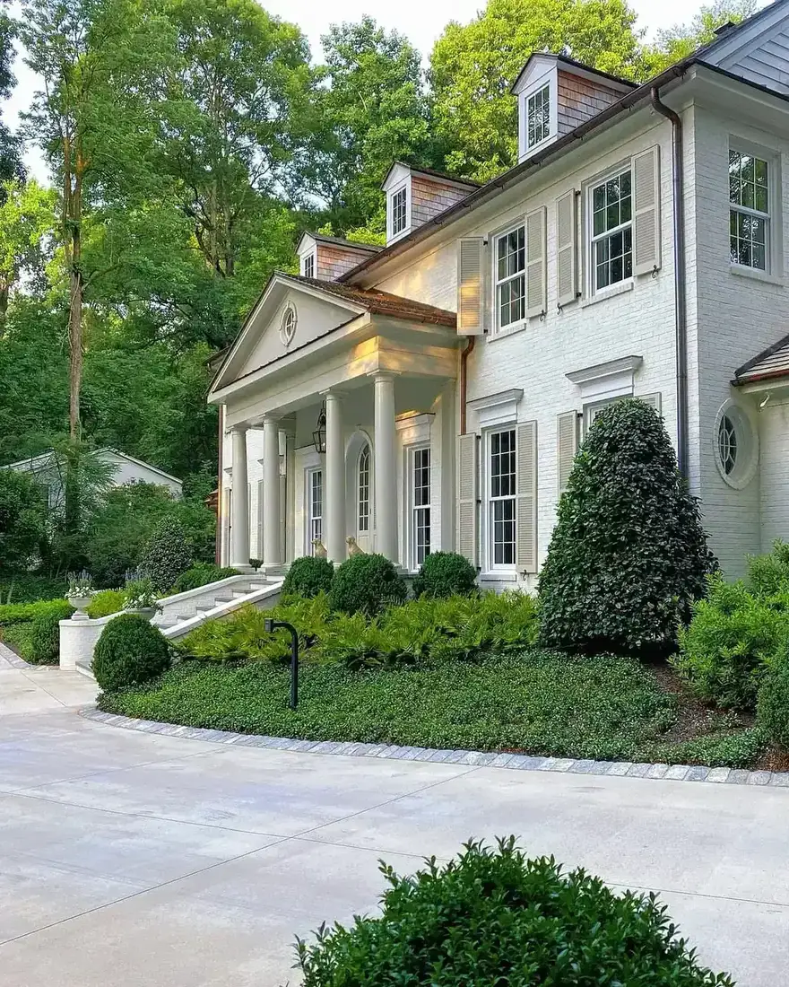 White brick colonial house with a columned porch and clipped boxwood either side of the door