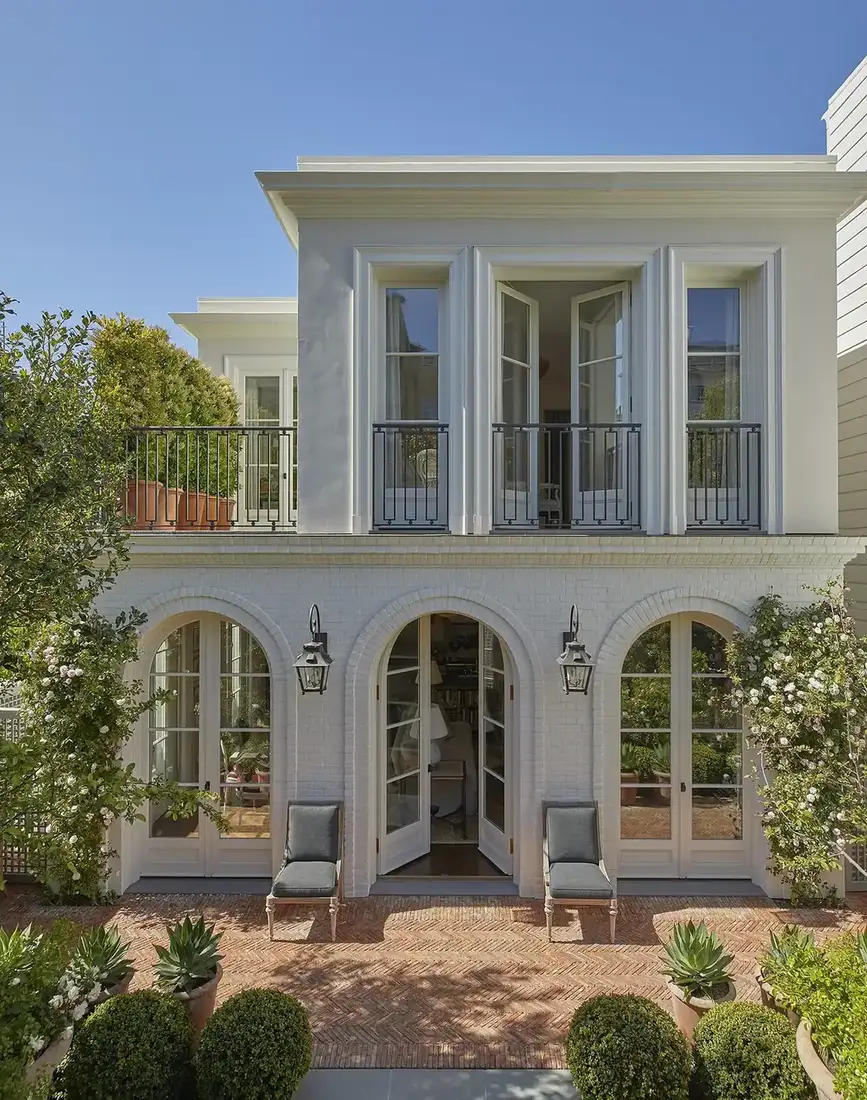 White brick house with arched French doors and a wrought iron balcony above