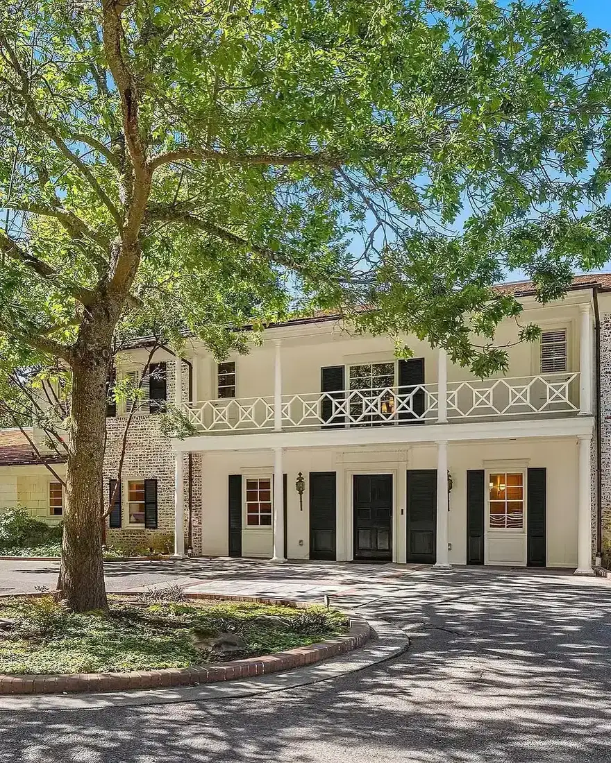 White brick house with a balcony, courtyard tree and structured evergreen planting
