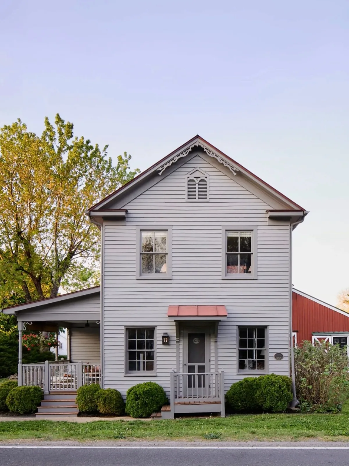 Gray farmhouse with a red barn and copper awning