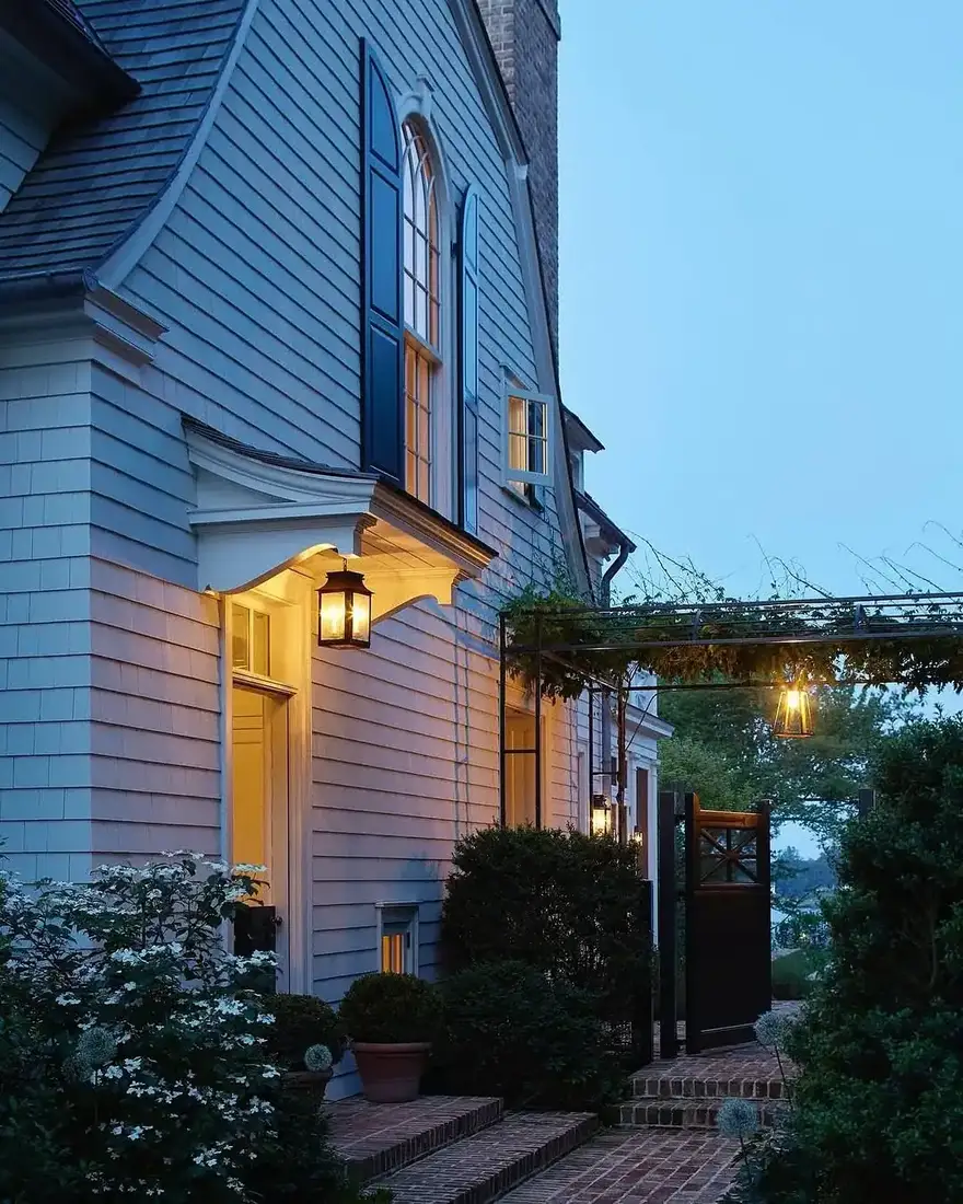 Blue shingle house at evening with warm lantern light over the porch