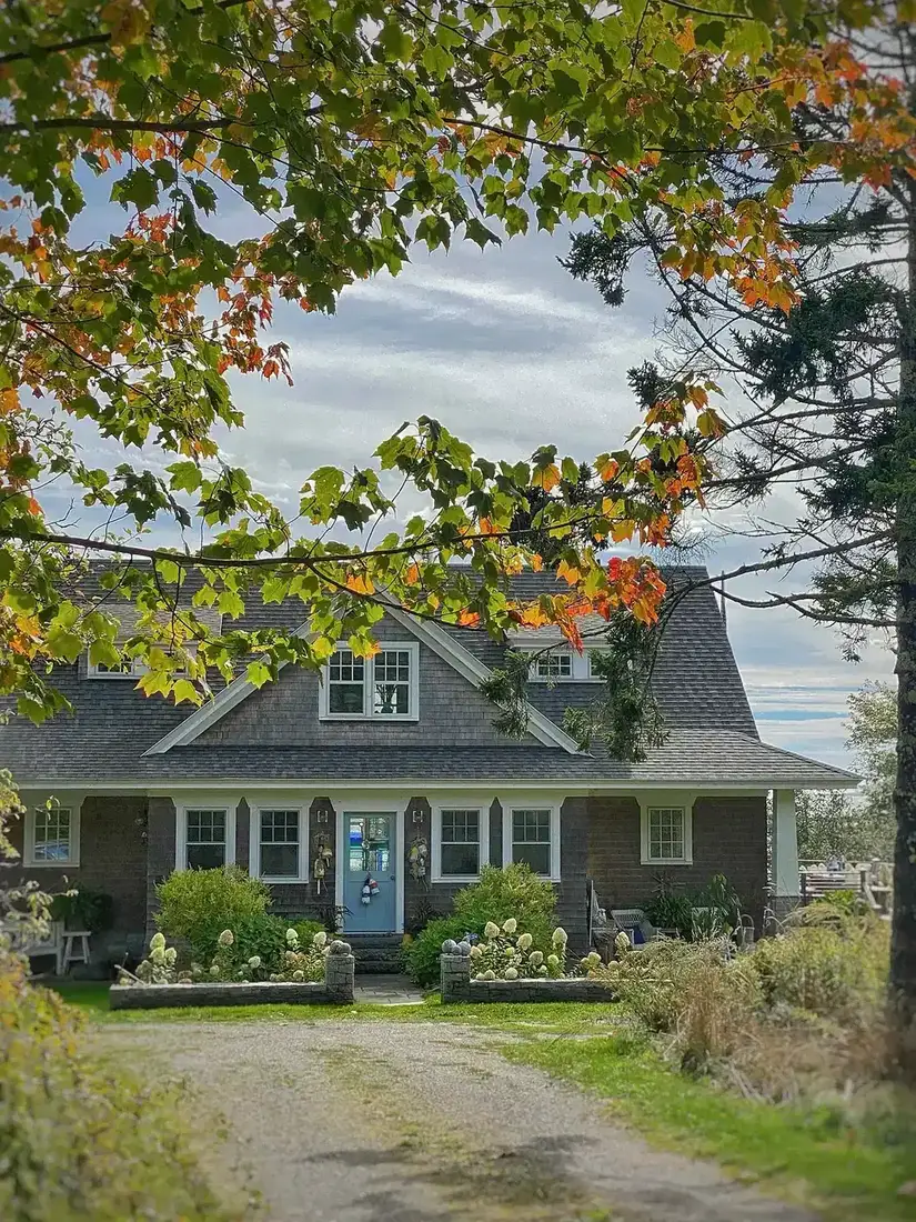 Brown shingle Dutch colonial house with gravel driveway and clipped lawn