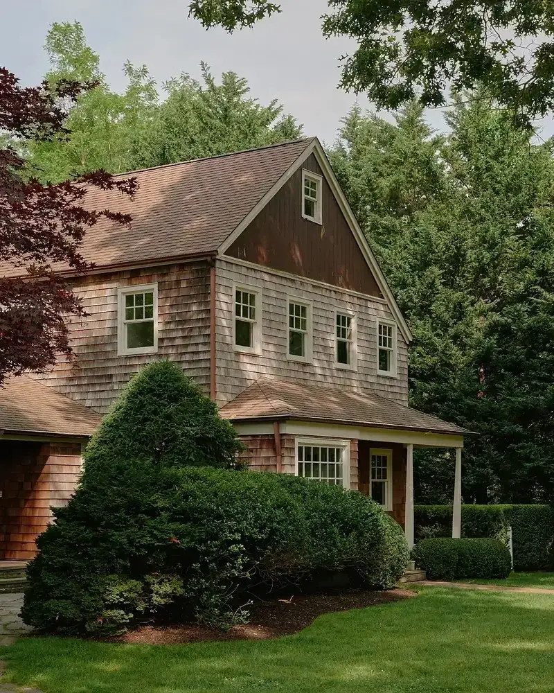 Brown gambrel shingle house set behind a wide green lawn