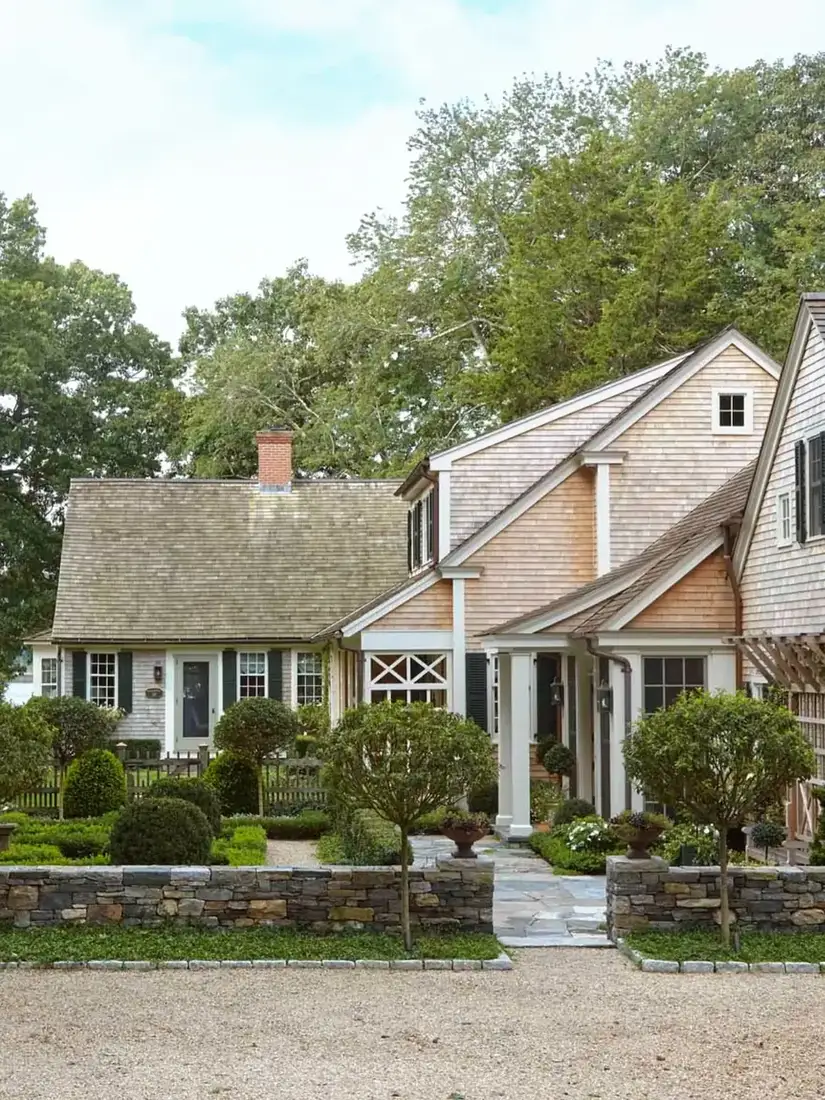 Cedar shingle Cape style house with stone wall and clipped topiary